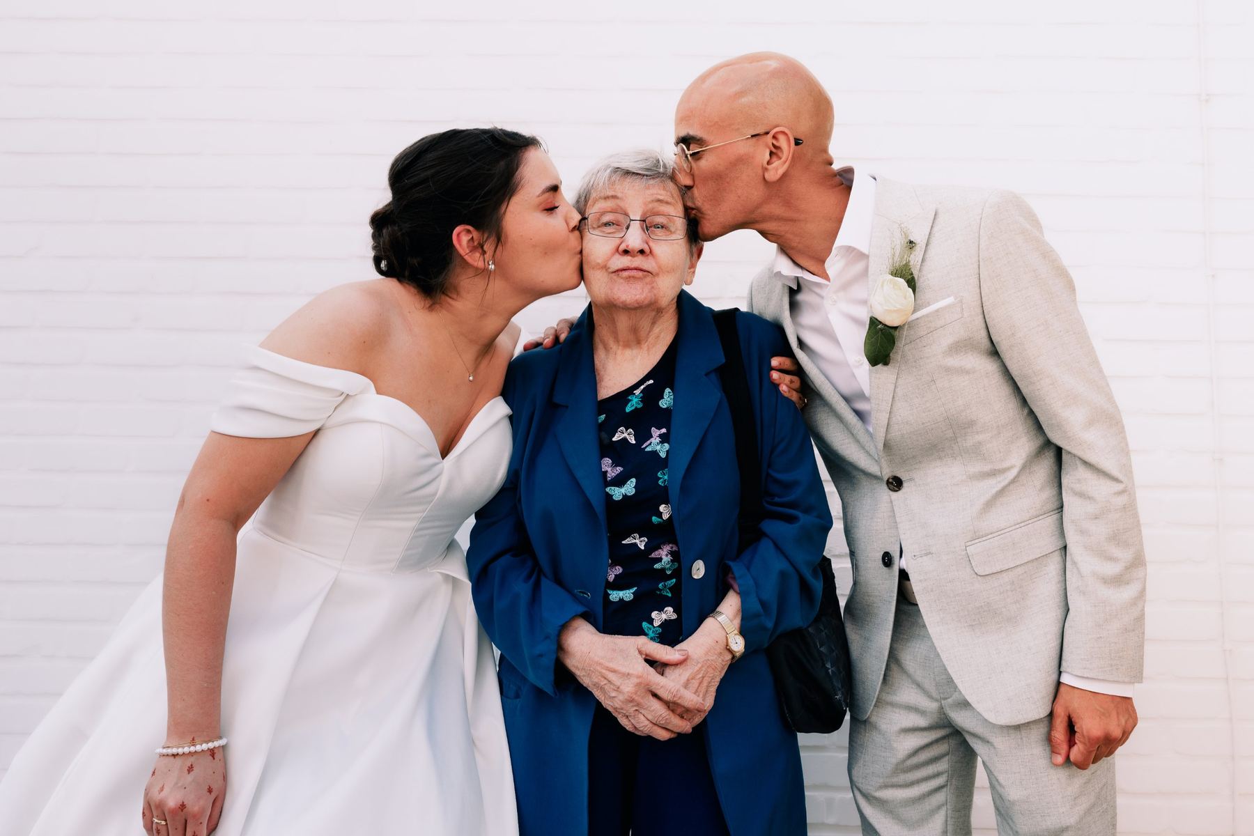 Bride and groom kissing grandma on both cheeks
