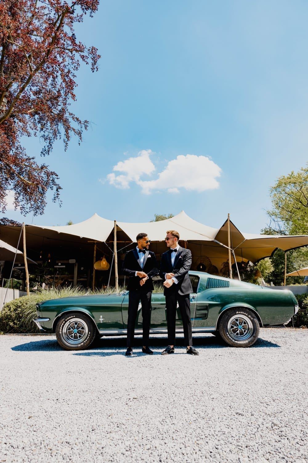 Groom and his best man in tuxedos beside a classic green Mustang