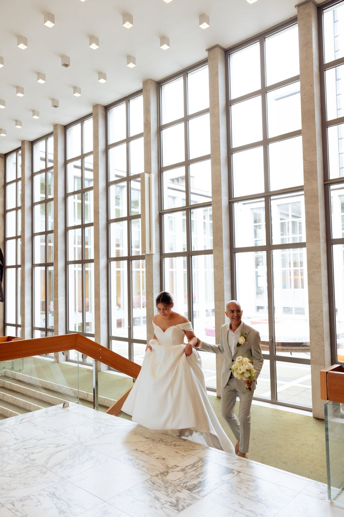 Bride and groom climbing a marble staircase in a bright hall