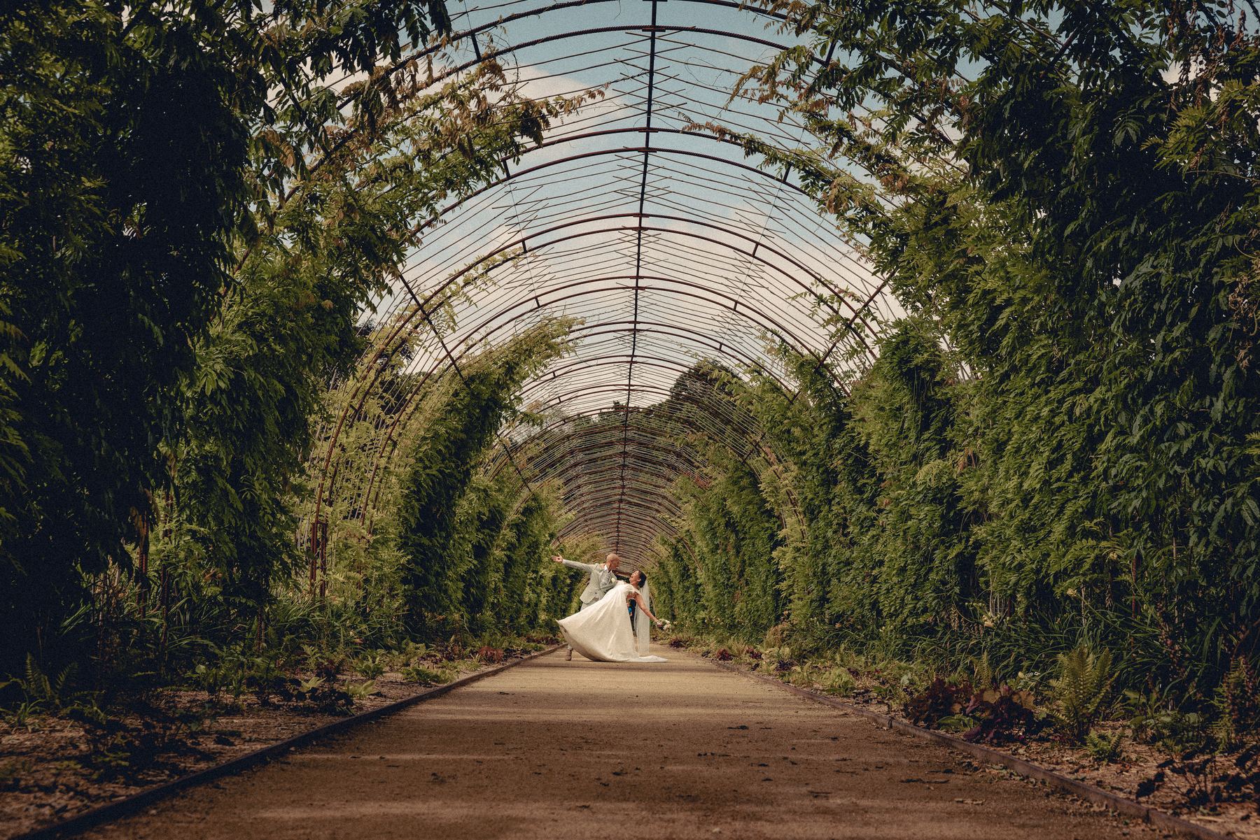 Bride and groom walking under a long green garden arch
