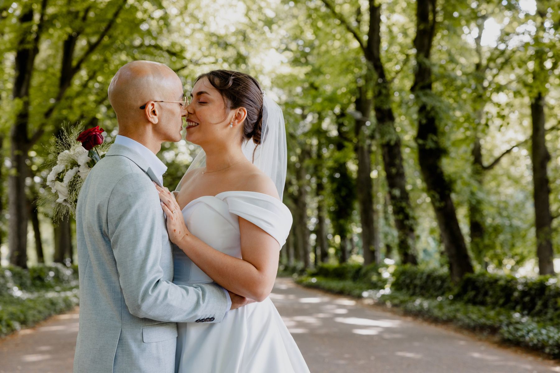 Bride and groom nose to nose in a tree-lined lane