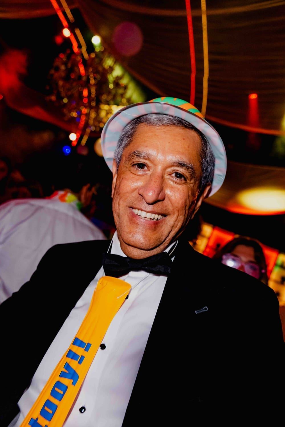 A wedding guest in a party hat and tuxedo, grinning at the party